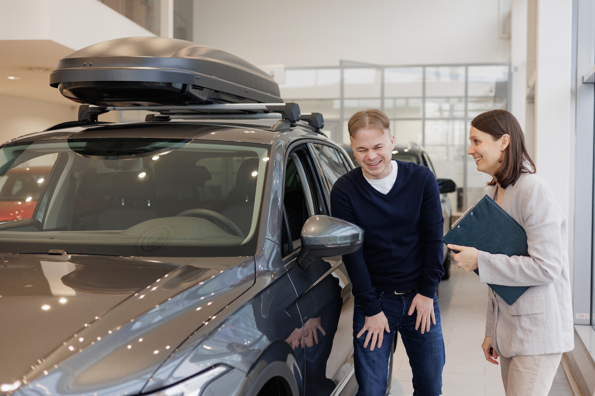 man buys a car at a car dealership. A female salesperson and car rental helps with the purchase
